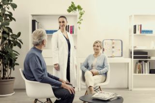 A couple having a meeting with an Amplifon hearing professional wearing a white coat