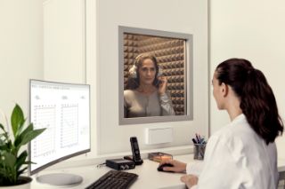 A woman taking a hearing screening in a booth at an Amplifon center