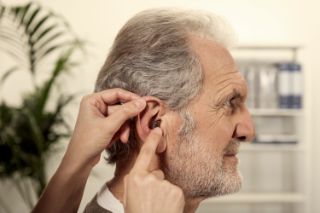 A hearing professional placing an ITE hearing aid inside a senior man's right ear