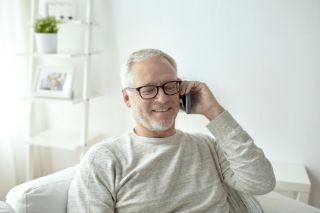 An elderly man smiling sitting on a couch and talking on the phone