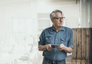 A senior man with glasses holding a pad and looking away