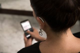 A senior woman wearing a hearing aid on her left ear looking at something on her smartphone