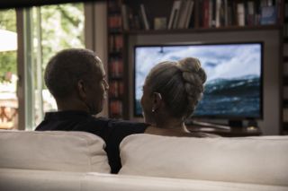 Couple sitting on the sofa and watching tv while wearing a hearing aid