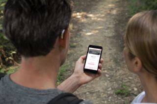 Un hombre usa una aplicación en su teléfono inteligente con su esposa al lado, en el campo