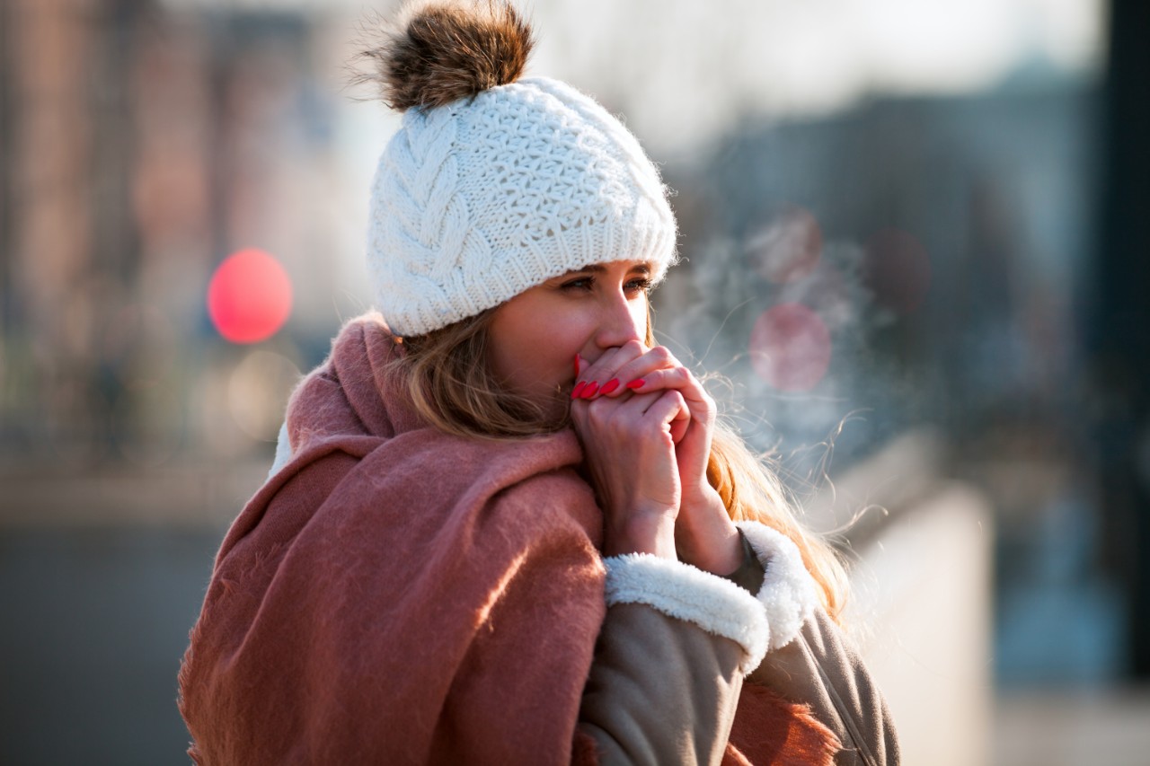 A woman with a hat warms her hands in winter