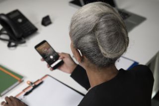 Una mujer de edad avanzada en el trabajo con un audífono mirando algo en su teléfono