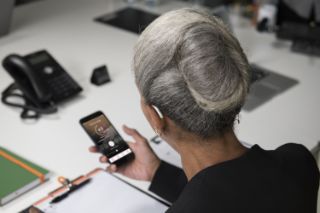 A senior woman wearing a hearing on her left ear using an app on her smartphone