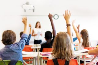 Niños en un aula levantando las manos