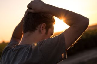 A man facing the sun at sunset with his hands on his head