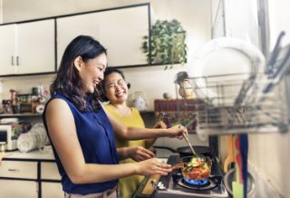A daughter and her mother smiling and laughing cooking together