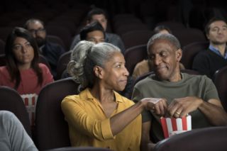 A senior couple watching a film in a theater eating popcorn