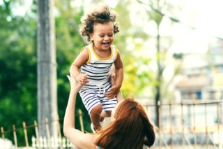 Mother with red hair lifting up in the air her smiling child 