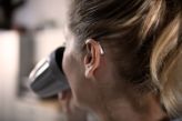 A woman wearing an hearing aid on her left ear drinking out of a mug