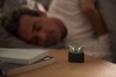 Man sleeping in his bed with rechargeable hearing aids in their charger on the nightstand