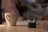 Rechargeable hearing aids on a table next to a cup
