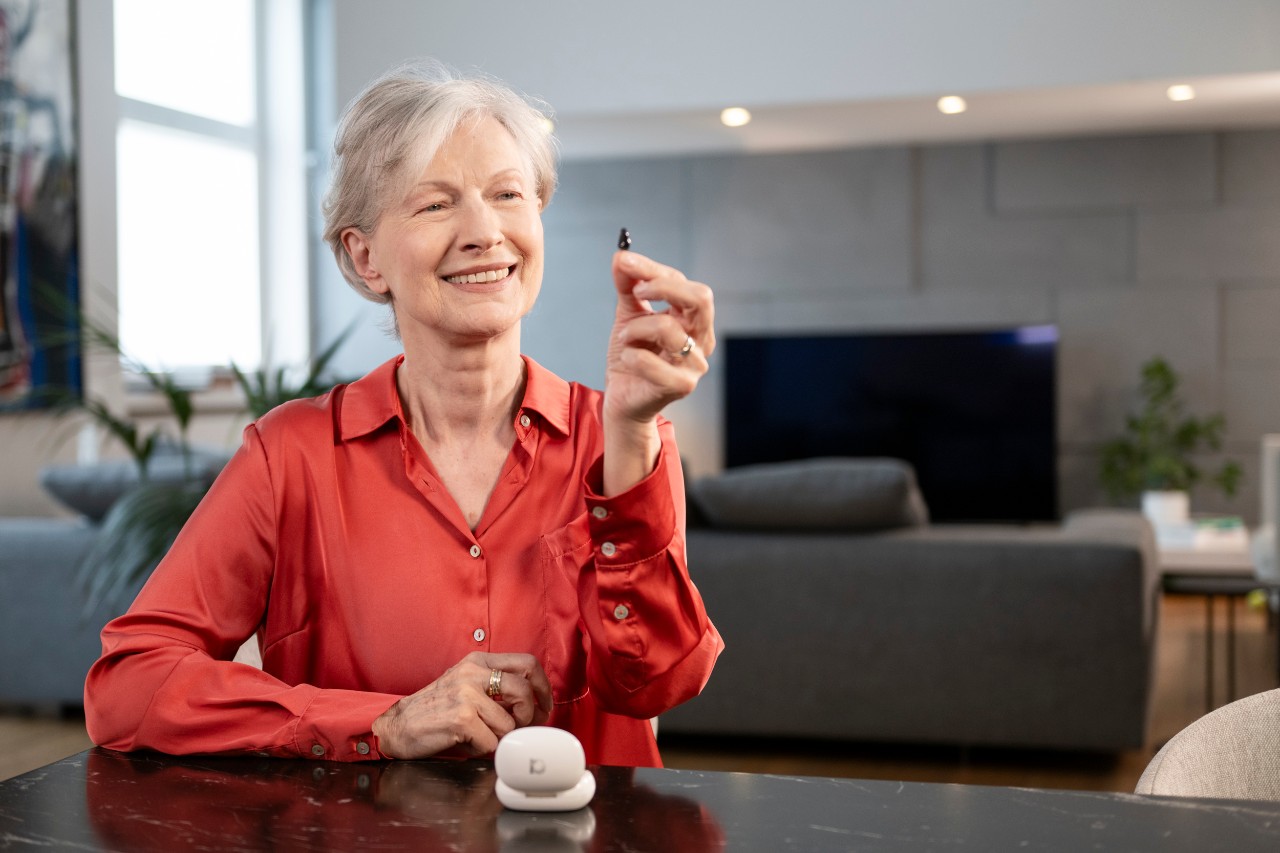 Senior woman holding a mini hearing aid and smiling