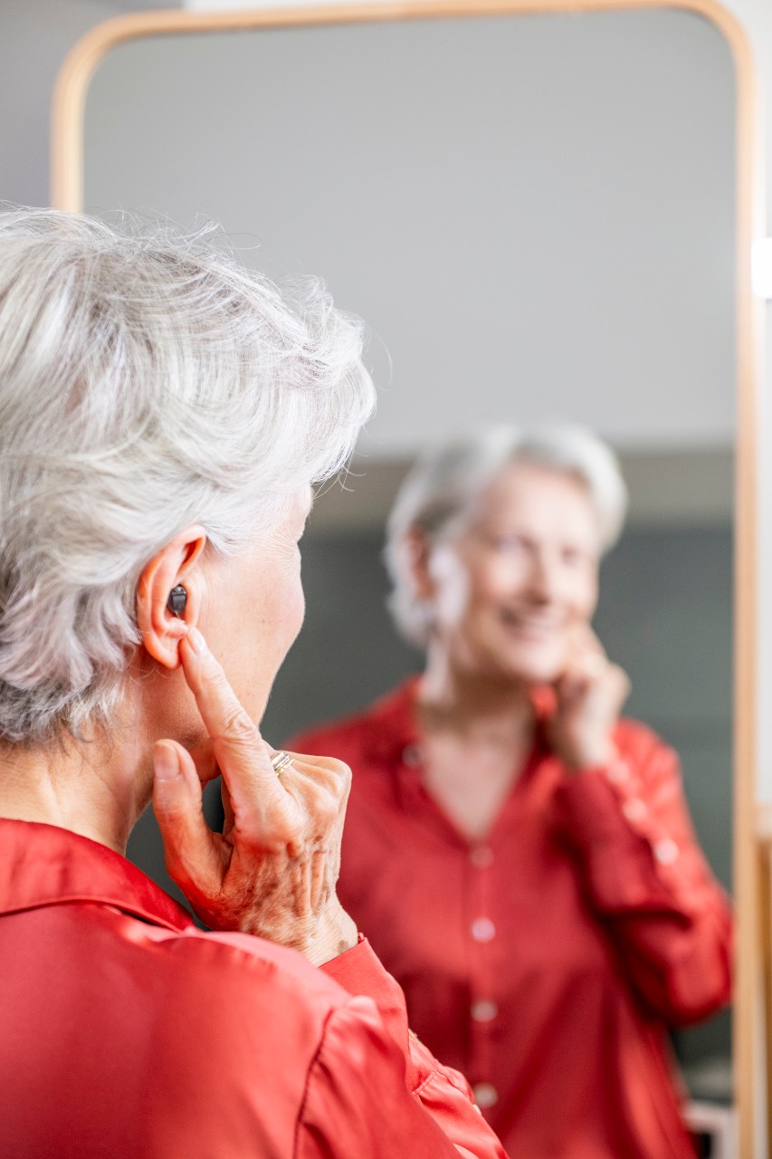 Elderly woman smiling at herself in the mirror while wearing hearing aids