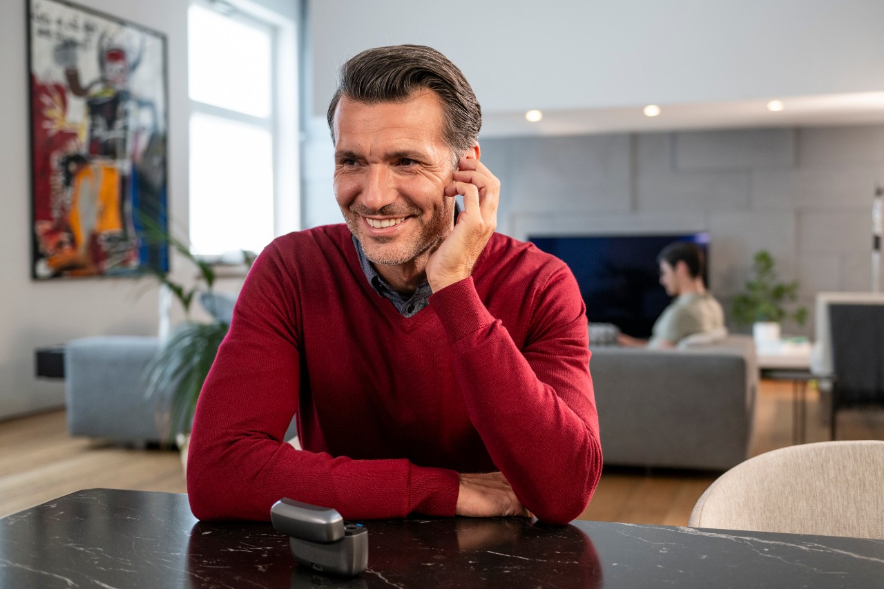 Man wearing red sweather touching his hearing aid