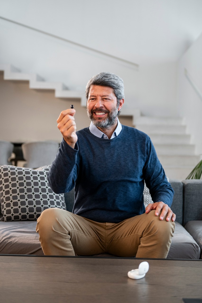 man inserting hearing aid and smiling