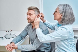 Provider placing hearing aid in man's ear