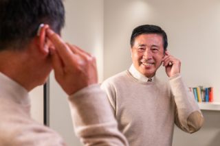 A man smiling while touching his hearing aid
