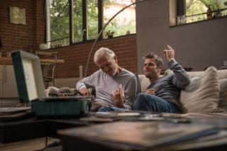 A senior and a young man listening to music on their sofa