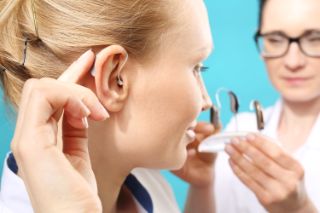 A woman placing a hearing aid in her ear.